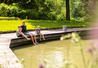 Gezin ontspant op houten steiger bij water bij De Witte Berg vakantiepark in Nederland op zonnige dag.