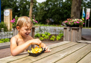 Ragazzo mangia patatine fritte a un tavolo di legno presso la tenda safari Tentvilla a De Witte Berg.