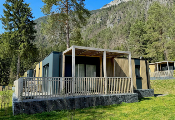 Buitenaanzicht van de moderne Wulfenia-lodge, omringd door bomen en bergen in een schilderachtige omgeving.