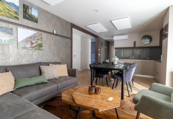 Soggiorno moderno con zona pranzo nella lodge Wulfenia al Pressegger See, Austria, con divano grigio e decori alle pareti.