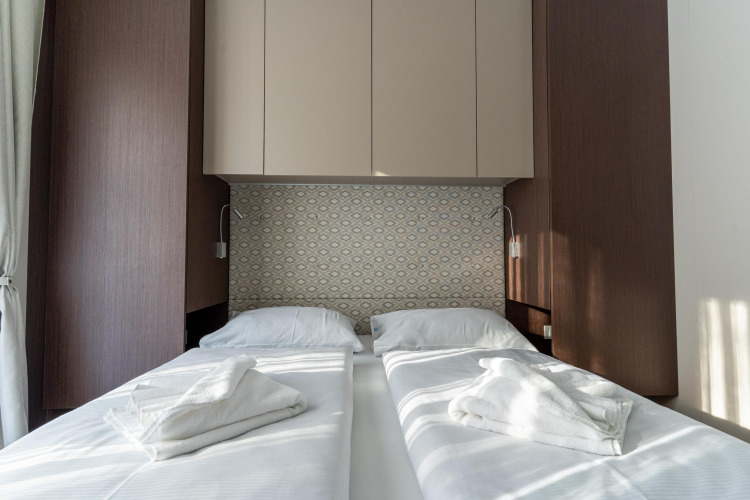 Habitación doble moderna con dos camas individuales, sábanas blancas y toques de madera en Wulfenia, Pressegger See, Austria.