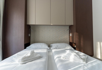 Chambre double moderne avec deux lits simples, linge blanc et éléments en bois à Wulfenia près du lac Pressegger, Autriche.