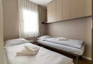 Habitación con dos camas individuales, decoración neutra y ventana en la cabaña Wulfenia en Pressegger See, Austria.