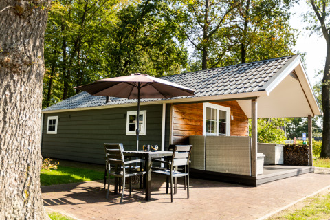 Knusse Forest Lodge op vakantiepark De Witte Berg in Nederland met terras, tafel en parasol buiten.