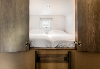 Sleeping area with two single beds behind wooden doors at Forest Lodge, Holiday park De Witte Berg, Netherlands.