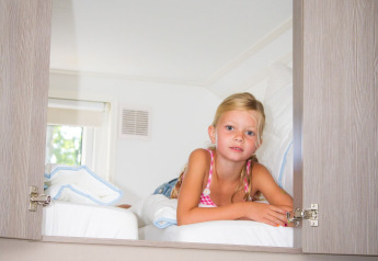 Bambina sdraiata su un letto nella Forest Lodge, Holiday park De Witte Berg, Paesi Bassi, arredo luminoso.
