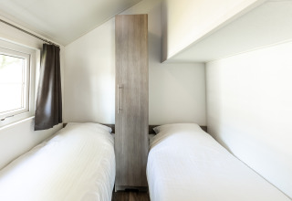 Habitación con dos camas individuales y armario en Forest Lodge, Holiday park De Witte Berg, Países Bajos.