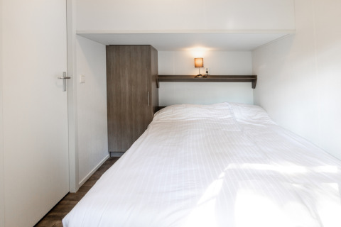 Modern bedroom in Forest Lodge at Holiday park De Witte Berg, Netherlands, with white bedding and wardrobe.