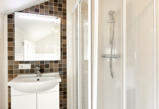 Heldere badkamer met wastafel, spiegel en douche in Forest Lodge op Vakantiepark De Witte Berg, Nederland.