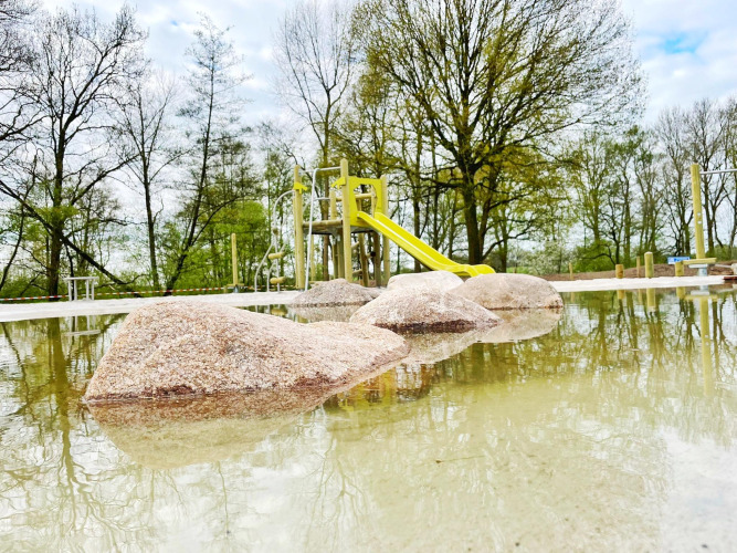 Rocas en aguas poco profundas frente a un parque con tobogán en Forest Lodge, De Witte Berg, Países Bajos, primavera.
