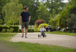 En mand går ved siden af et lille barn på en trehjulet cykel i Forest Lodge, De Witte Berg, Holland.