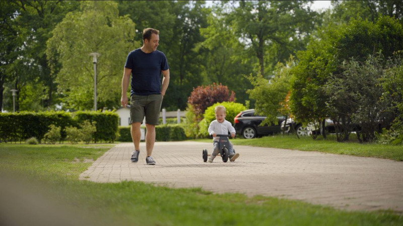 Een man loopt naast een jong kind op een driewieler bij Forest Lodge, De Witte Berg, Nederland.