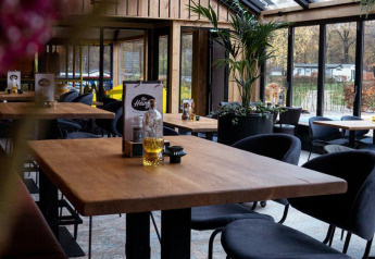 Modern lodge-interieur met houten tafels, zwarte stoelen en planten in Forest Lodge, De Witte Berg, Nederland.