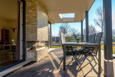 Terraza exterior con mesa de comedor, sillas y chimenea en villa vacacional y sauna en Holiday park Ackersate.