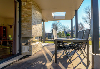 Terraza exterior con mesa de comedor, sillas y chimenea en villa vacacional y sauna en Holiday park Ackersate.