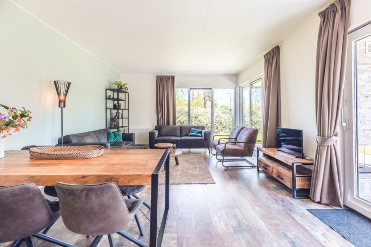 Helles Wohnzimmer mit Holzmöbeln, großen Fenstern und Naturblick in einer niederländischen Ferienvilla.