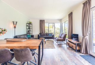 Soggiorno moderno in villa vacanze con arredi in legno, ampie finestre e vista giardino in Olanda.