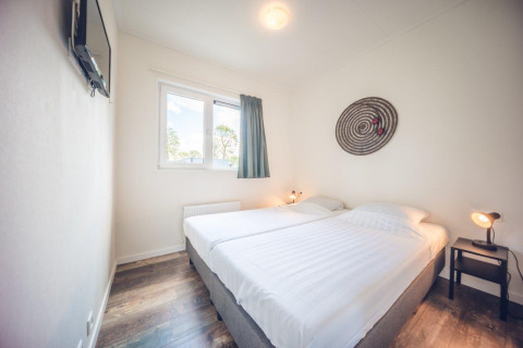 Soveværelse med to enkeltsenge, moderne indretning, vindue og vægdekoration i Holiday park Ackersate, Holland.