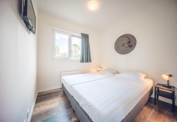 Camera da letto con due letti singoli, arredo minimale, finestra e lampada a Holiday park Ackersate, Paesi Bassi.