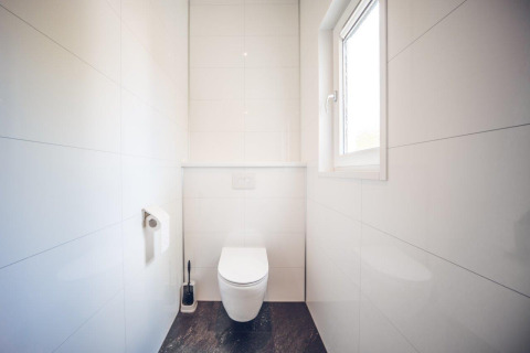 Et lyst og moderne toilet med vindue, vægmonteret toilet og toiletpapir i feriebolig på Holiday park Ackersate.