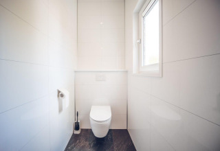 Et lyst og moderne toilet med vindue, vægmonteret toilet og toiletpapir i feriebolig på Holiday park Ackersate.