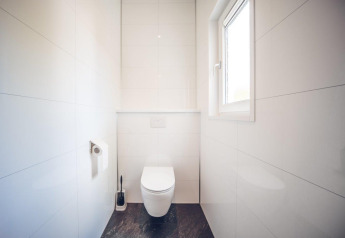 Et lyst og moderne toilet med vindue, vægmonteret toilet og toiletpapir i feriebolig på Holiday park Ackersate.