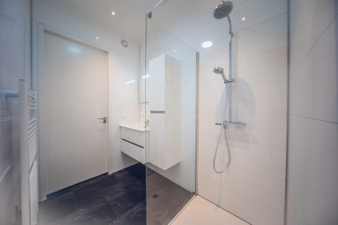 Baño moderno con ducha acristalada y baldosas blancas en Vacation villa + sauna en Holiday park Ackersate.