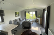 Interior del Chalet Brilon en Camping & Ferienpark Brilon, Alemania, con sofá, mesa de comedor y ventanas grandes.