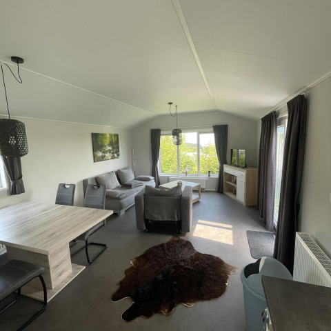 Interior del Chalet Brilon en Camping & Ferienpark Brilon, Alemania, con sofá, mesa de comedor y ventanas grandes.