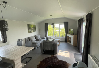 Interior del Chalet Brilon en Camping & Ferienpark Brilon, Alemania, con sofá, mesa de comedor y ventanas grandes.