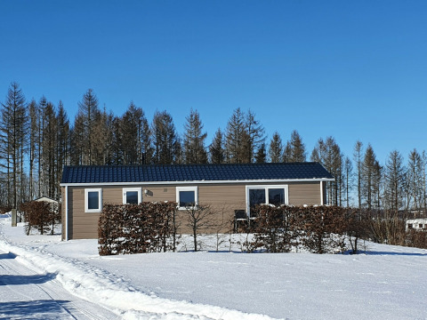 Cabaña Chalet Brilon en Camping & Ferienpark Brilon en Alemania, rodeada de nieve y árboles bajo un cielo azul.