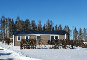 Cabaña Chalet Brilon en Camping & Ferienpark Brilon en Alemania, rodeada de nieve y árboles bajo un cielo azul.