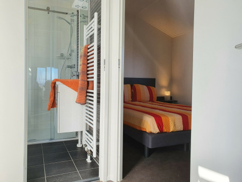 Dormitorio y baño modernos en Chalet Brilon, Camping & Ferienpark Brilon, Alemania, con detalles en naranja.