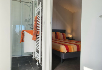 Dormitorio y baño modernos en Chalet Brilon, Camping & Ferienpark Brilon, Alemania, con detalles en naranja.