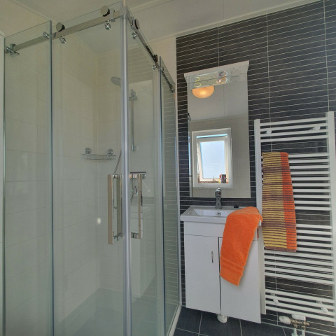 Baño moderno en Chalet Brilon con ducha de vidrio, lavabo blanco y toallas naranjas en el radiador.