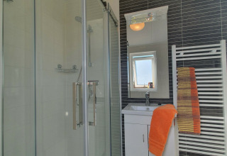 Baño moderno en Chalet Brilon con ducha de vidrio, lavabo blanco y toallas naranjas en el radiador.