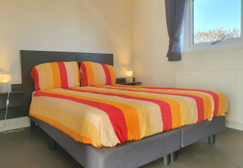 Dormitorio con cama doble y ropa de cama a rayas de colores en Chalet Brilon en Camping & Ferienpark Brilon en Alemania.