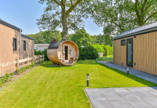 Buitenzicht van een luxe lodge met houten gevel en barrelsauna in de tuin bij Drentse Weelde, Nederland.