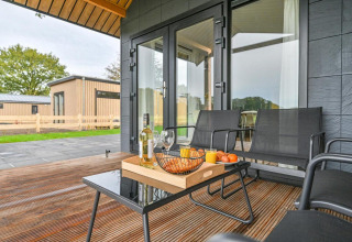 Terraza exterior de una lujosa cabaña en Drentse Weelde, Países Bajos, con vino, snacks y asientos modernos.
