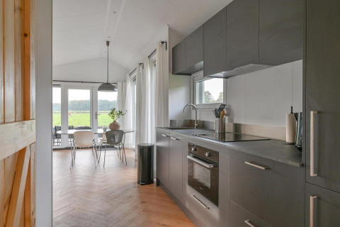 Modern lodge kitchen with gray cabinetry and dining area in the Luxury lodge at Drentse Weelde, Netherlands.