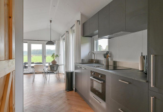 Modern lodge kitchen with gray cabinetry and dining area in the Luxury lodge at Drentse Weelde, Netherlands.