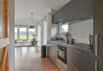 Moderne lodgekøkken med grå skabe, spiseområde og store vinduer på Drentse Weelde i Holland.