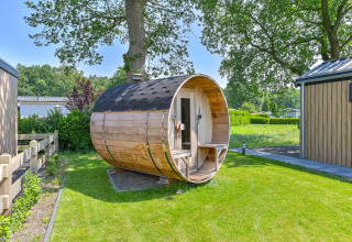 Sauna de madera en forma de barril junto a un lodge de lujo en Drentse Weelde, Países Bajos, rodeado de vegetación.