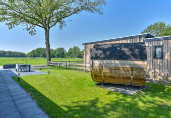 Outdoor view of a luxury lodge with sauna at Drentse Weelde in the Netherlands, set in a green landscape.