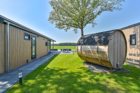 Casa de lujo y sauna exterior en Drentse Weelde, Países Bajos, rodeada de césped y naturaleza.
