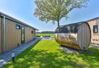Luxus-Lodge mit Außensauna bei Drentse Weelde in den Niederlanden, umgeben von Rasen und Bäumen.
