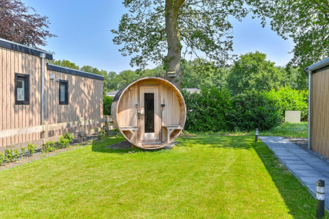 Foto exterior de una cabaña de lujo con sauna de barril en Drentse Weelde, Países Bajos, rodeada de vegetación.