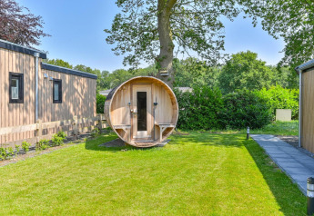 Outdoor photo of a luxury lodge with a barrel sauna at Drentse Weelde, Netherlands, surrounded by greenery.