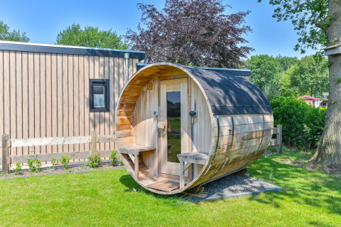 Luxury wooden lodge with a barrel-shaped outdoor sauna at Drentse Weelde, Netherlands, on a sunny day.