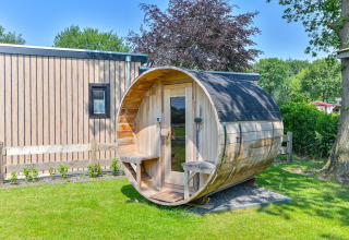 Luxuriöse Lodge mit einer fassförmigen Sauna im Garten in Drentse Weelde, Niederlande, bei Sonnenschein.